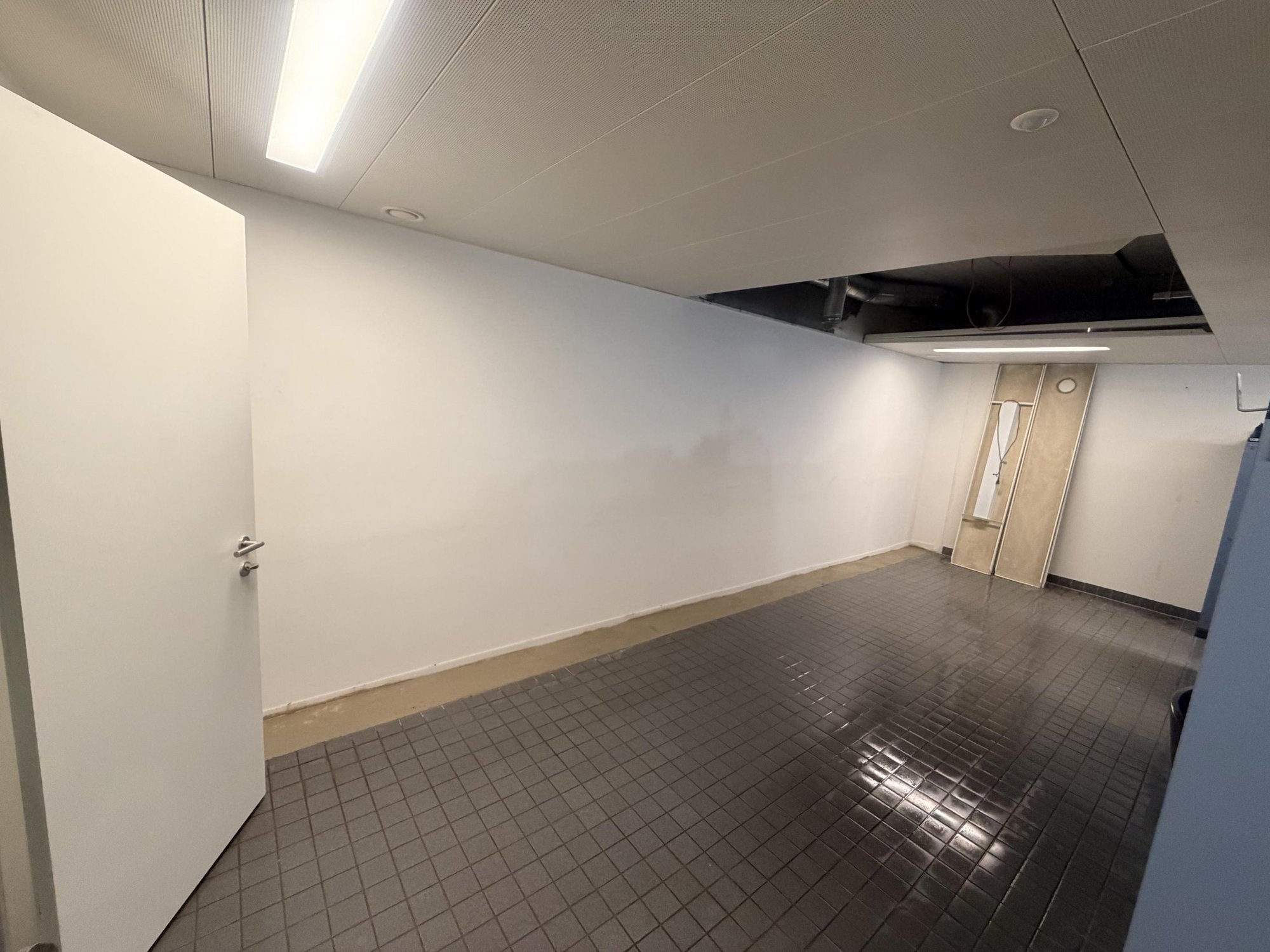 Leerer Raum mit weißer Decke, teils geöffneten Deckenplatten und grauem Fliesenboden